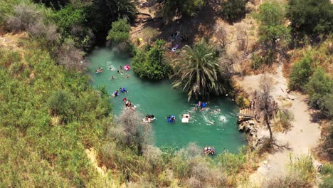 mucha gente flota en colchones de aire en un cálido día soleado en el manantial natural azul claro mientras los jóvenes se sumergen con entusiasmo desde una plataforma en el agua