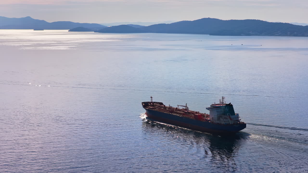 Aerial drone view of an oil tanker traveling across open Adriatic waters with distant mountain ridges and coastal towns visible on the horizon
