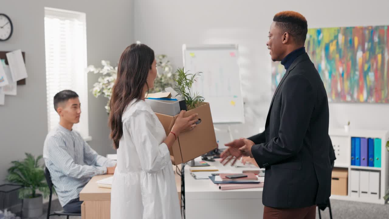 A smartly dressed manager welcomes an ambitious new talent woman who keeps accessories in a cardboard box, the man shakes the girl's hand and congratulates her on the job