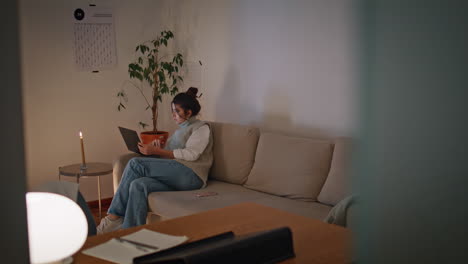 serious woman working laptop sitting sofa evening home. lady studying remotely