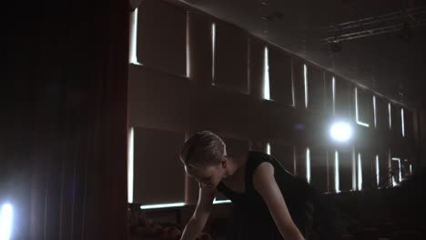 Middle-plan-slow-motion:-a-Young-ballerina-girl-performs-graceful-movements-on-the-stage-in-a-tutu-and-Pointe-shoes-in-the-dark-and-smoke.