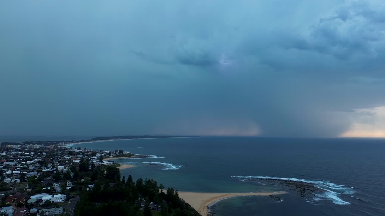 Drone aerial landscape of stormy weather with heavy rainfall and bright lightning strikes across the sky above the coastline at Toowoon Bay Beach Central Coast Australia nature environment climate