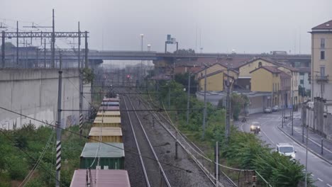 Cargo-train-pulling-carts-in-suburbs-of-Milan-city,-handheld-view