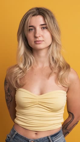 serious young woman standing with hands behind on yellow background