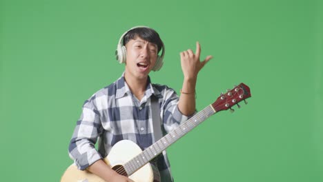 young asian teen boy wearing headphone with guitar and rapping on the green screen background