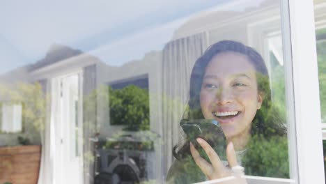 Happy-asian-woman-talking-on-smartphone-and-looking-through-window,-in-slow-motion