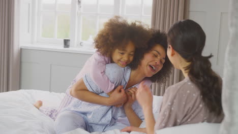 family with two mums wearing pyjamas playing on bed at home with daughter