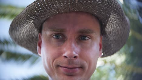 man wearing a straw hat against a lush outdoor background featuring blurred foliage and sunlight.