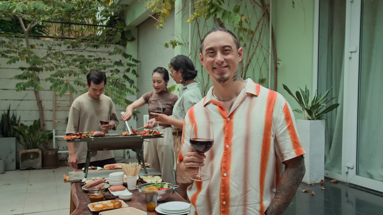 Portrait of Cheerful Tattooed Man with Wine Barbecuing with Friends
