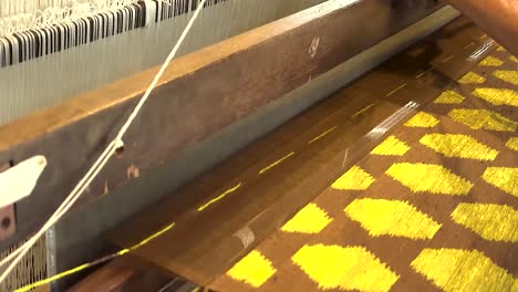 close-up of hands weaving vibrant yellow patterns on a traditional loom.