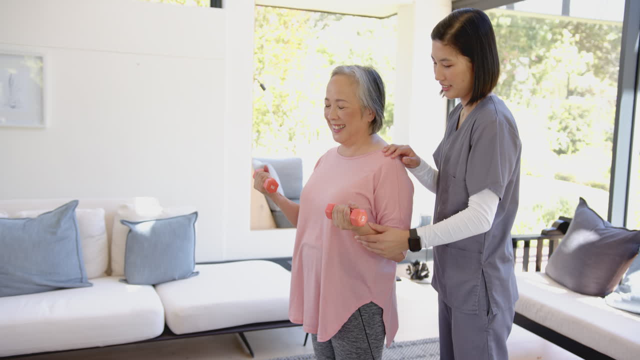 Senior asian woman exercising with dumbbells, assisted by physiotherapist at home