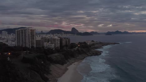 enfoque aéreo de una pequeña playa con el fuerte de copacabana en primer plano y la montaña sugarloaf en el fondo contra un amanecer de color nublado