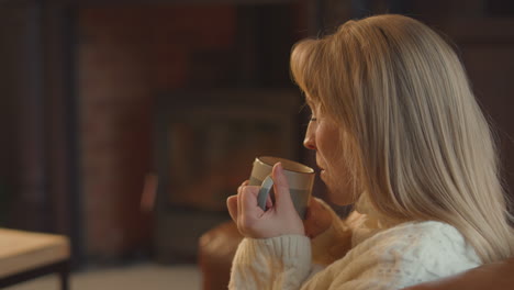 woman at home in lounge with cosy fire with hot drink