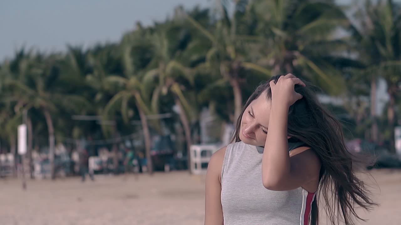 행복한 소녀는 열대 해변에서 어두운 머리카락을 고정합니다. 느린 동작