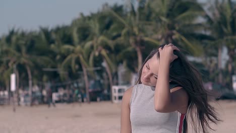 happy girl fixes dark hair on tropical beach slow motion