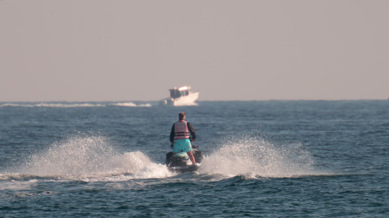 Cannes, France - October 10, 2025: A man on a jet ski speeds across the sparkling blue waters of the French Riviera with a yacht in the background