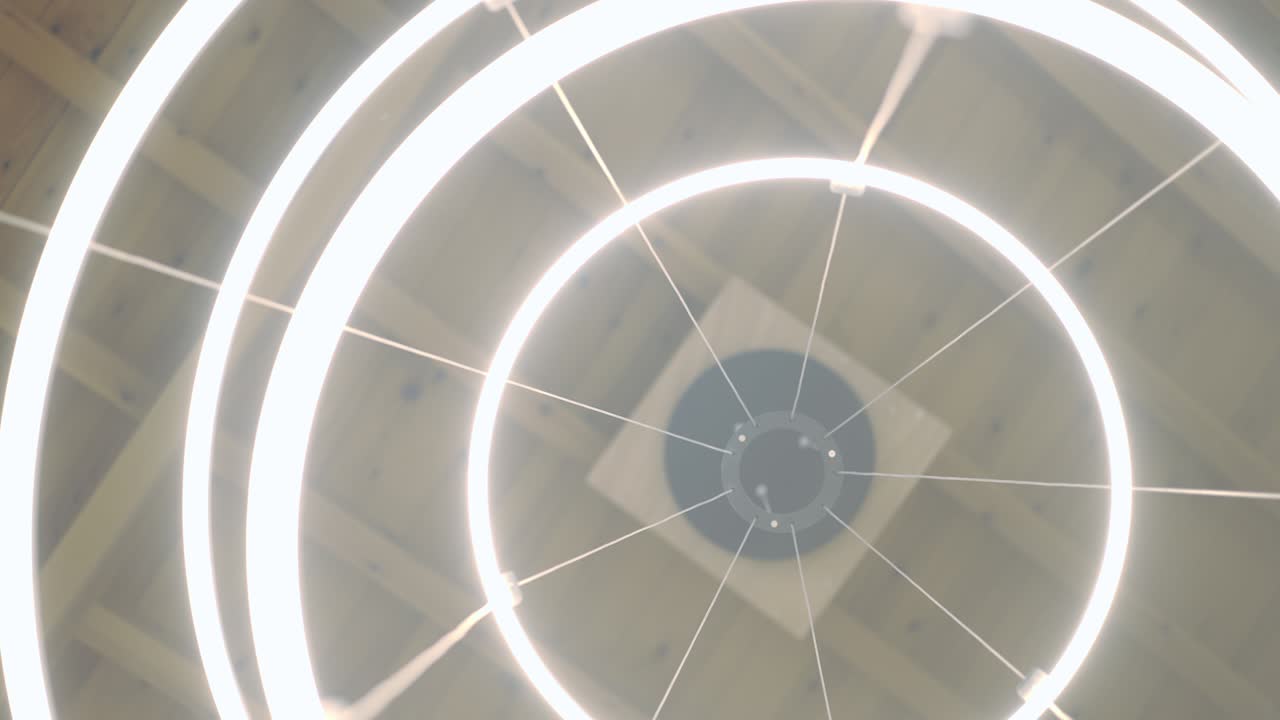 vista de abajo elegante candelabro iluminado colgando del techo en el interior. círculos redondos de primer plano brillando con luz fría en el hogar o la tienda. cámara en vivo girando en cámara lenta.