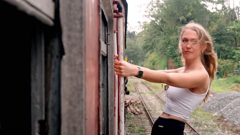 a young woman leans gracefully out of the door of a vibrant blue train as it winds through the lush green landscapes of sri lanka's iconic ella to kandy route.