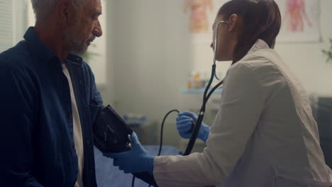 woman cardiologist measuring pressure senior patient in hospital office closeup