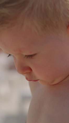 pensive little child boy with bare shoulders stands on public beach at contemporary marine resort on warm summer day closeup slow motion