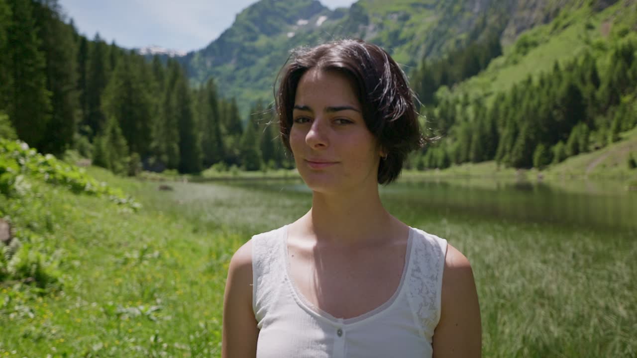 Glad kvinde med kort brunt hår smilende ind i kameraet. Smuk schweizisk natur med idyllisk landskab og bjerge. Solskinsdag. Portrætbillede