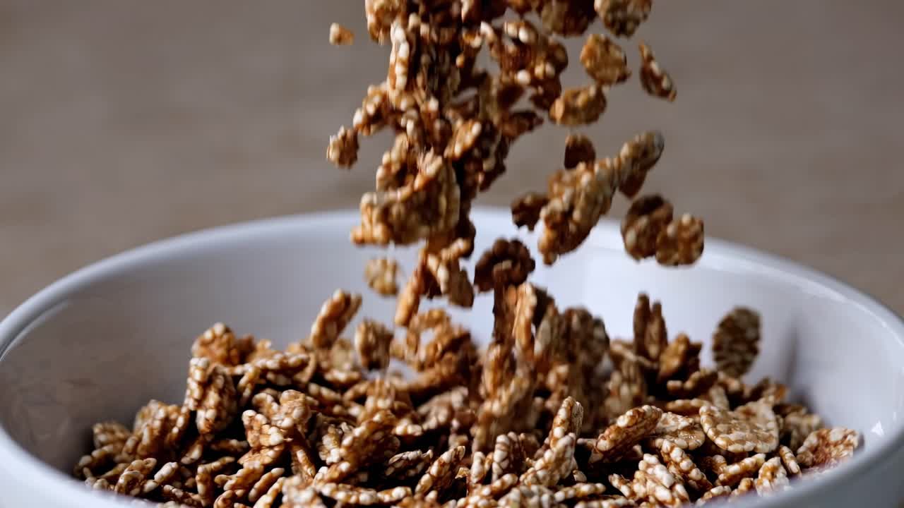 Video ravvicinato di granola che cade in una ciotola bianca, ripreso da un'angolazione laterale, che mostra dinamicità