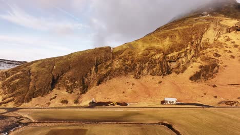 aerial view near skógafoss waterfall, iceland. rugged brown hillside meets flat land under a cloudy sky. stark nordic landscape.
