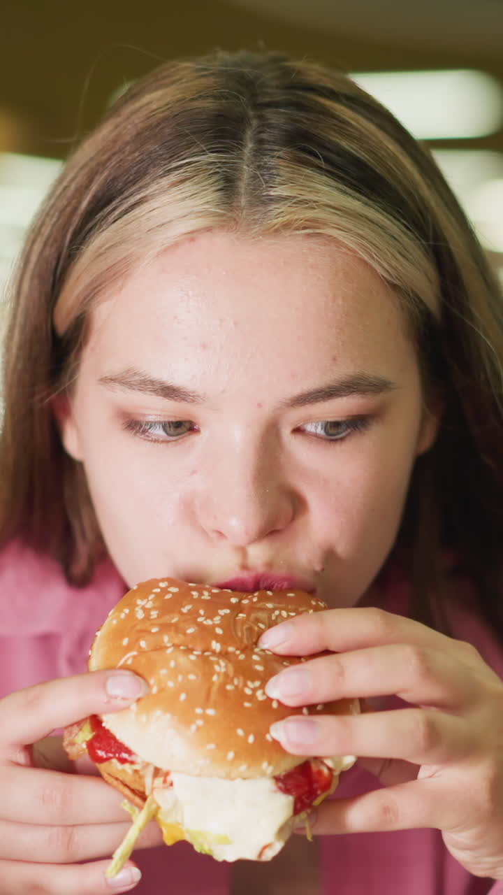 dama de vestido rosa toma un bocado de hamburguesa, masticando lentamente mientras contempla el sabor, se ve reflexiva mientras saborea la comida, el fondo presenta efectos de luz bokeh borrosos