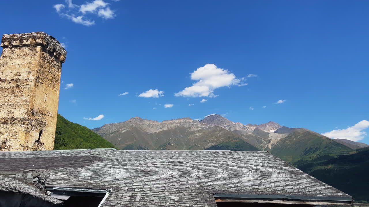 Historic stone towers of Mestia rise against the Caucasus mountains under a clear blue sky. A blend of medieval architecture, wooden houses, and scenic Georgian highland landscape
