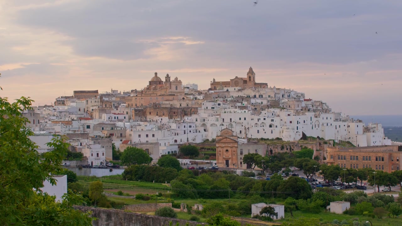 Ostuni, Provincia di Brindisi, Puglia, Italia, con architettura storica imbiancata a calce, la Cattedrale di Ostuni, strade medievali e uliveti ondulati sotto la luce soffusa del tramonto, inquadratura paesaggistica introduttiva