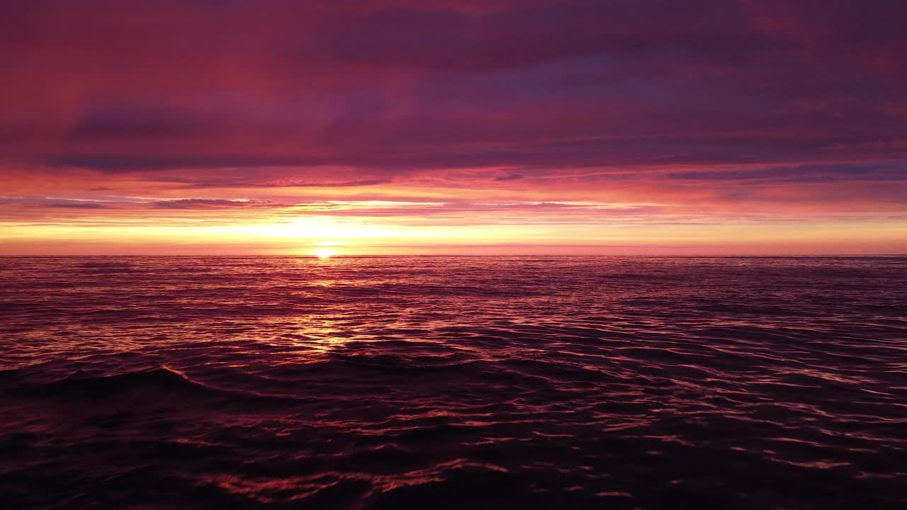 발트해의 아름다운 공중 생생한 고대비 분홍색 보라색 일몰, 카로스타 전쟁 항구 콘크리트 해안 요새 폐허 리파자, 넓은 각도의 드론 샷이 잔잔한 바다 위로 낮게 뒤로 이동