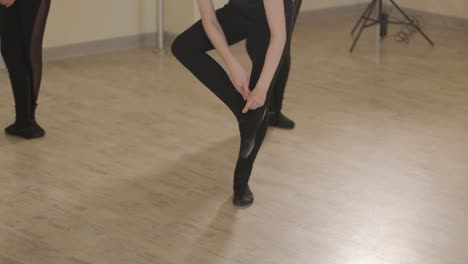 a group of young ballet students in black dancewear practicing positions in a spacious ballet studio with wooden flooring and wall-mounted barres. focused expressions and synchronized movements.