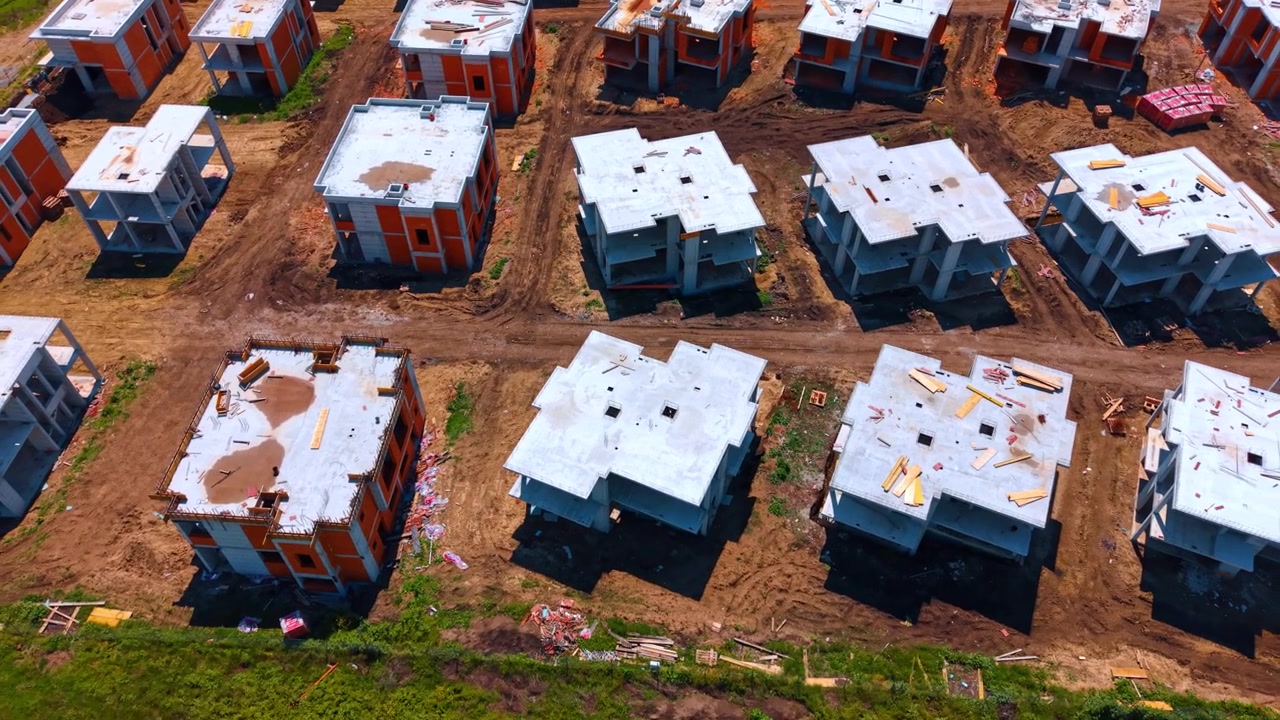 Vista dall'alto di case residenziali incompiute e cantiere. Vista aerea di strutture in cemento e mattoni di case in costruzione con strade sterrate.