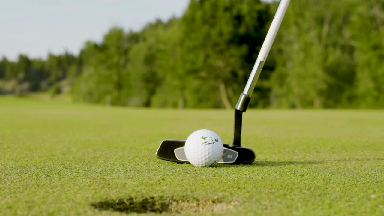 cámara lenta cerca de un putter golpeando una pelota de golf y hundiendo un putt corto