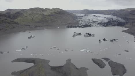 Aerial-view-overlooking-ice-blocks-and-the-Solheimajokull-glacier---tilt,-drone-shot