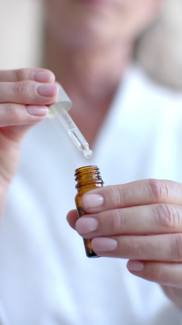 Vertical video: Using dropper bottle, woman applying essential oil at home for skincare