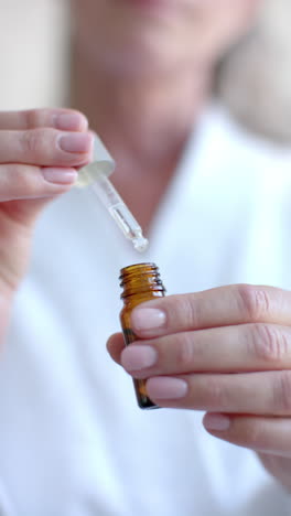 vertical video: using dropper bottle, woman applying essential oil at home for skincare