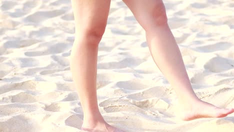Close-up of bare legs playfully moving on sunlit sandy beach.