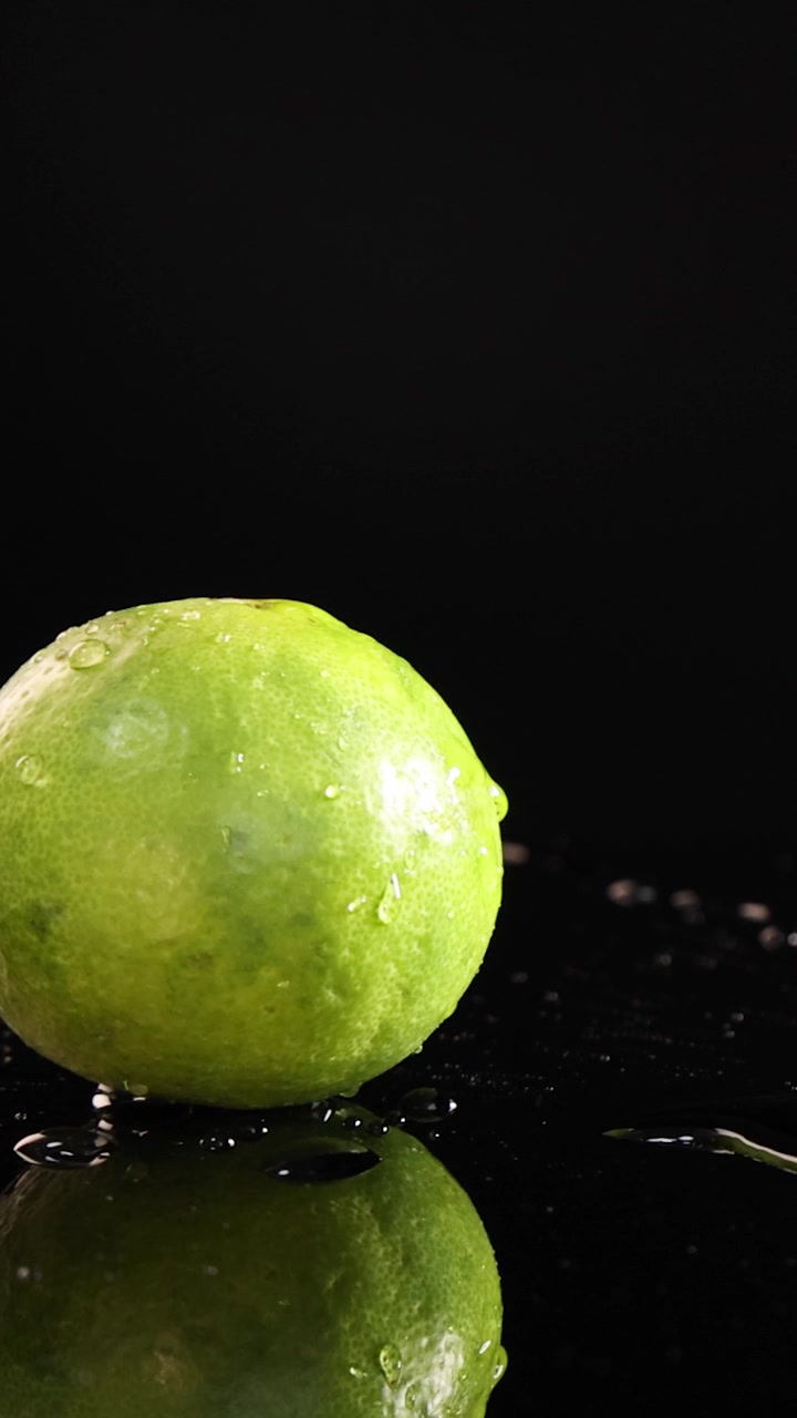 Un lime verde intero cade e rimbalza su una superficie nera bagnata e riflettente, ripreso al rallentatore con illuminazione drammatica e dettagli nitidi