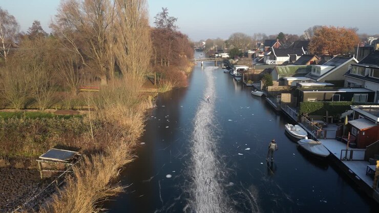 Veduta aerea di membri della comunità che pattinano sul ghiaccio su un fiume ghiacciato a Hendrik-Ido-Ambacht, Paesi Bassi.
