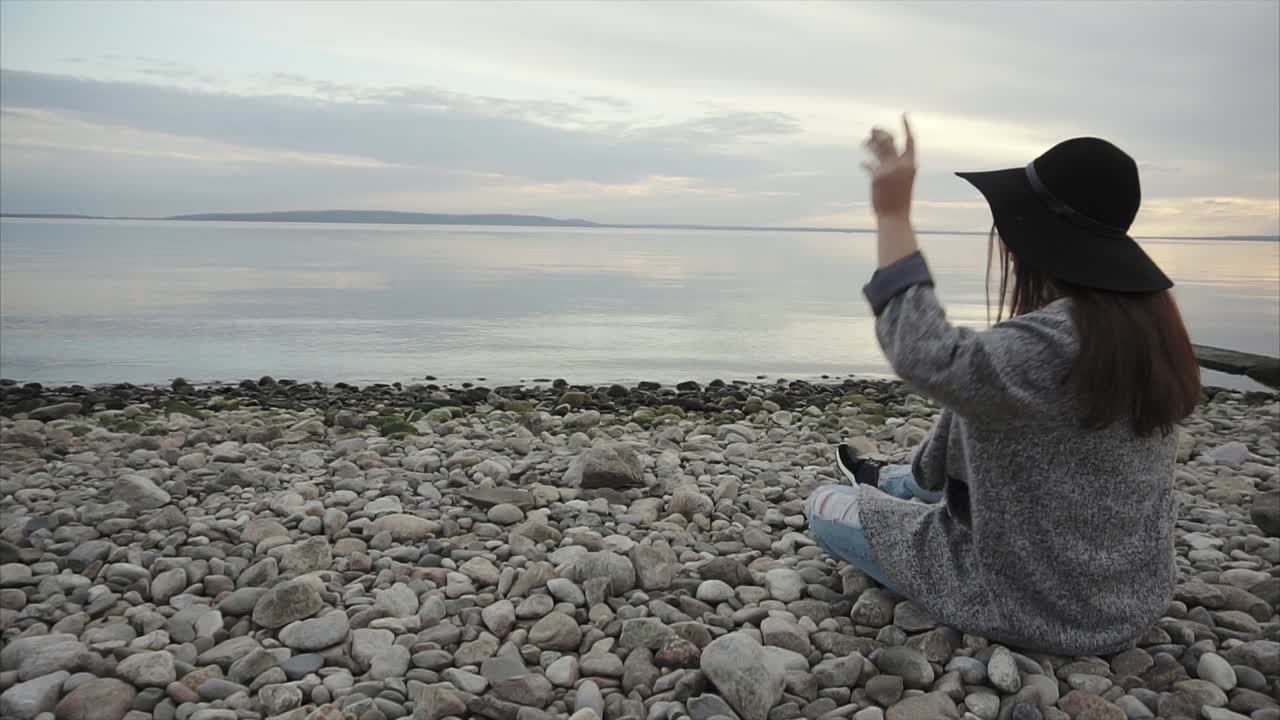 Woman Sitting on a Pebble Beach at Sunset
