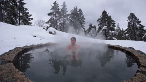 person soaking in a steaming outdoor hot spring during winter