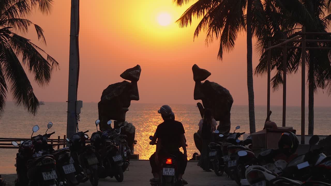 Local residents enjoy a beautiful sunset on Phu Quoc Island, driving scooters with their hands in the air, embracing the moment and life’s simple pleasures while surrounded by the ocean.