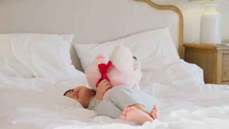 una niña jugando en la cama con pijama en casa acurrucando un juguete blando