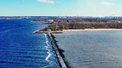 daugavgrīva lighthouse and its stone breakwater at the confluence of the daugava river and the baltic sea, riga, latvia, in early spring, under a bright azure sky with sparse white clouds