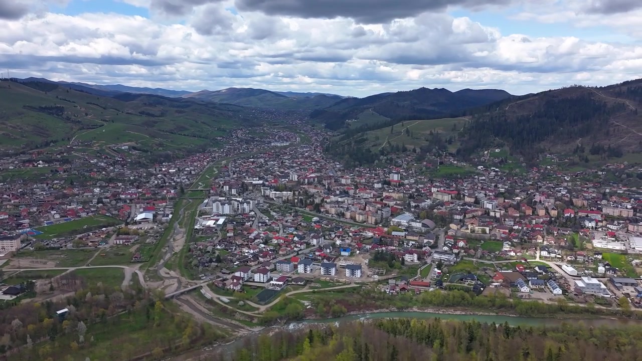 Hyperlapse aereo della città di Gura Humorului circondata da montagne e foreste sotto nuvole drammatiche in Romania.