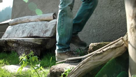 hombre anónimo con jeans y botas subiendo las escaleras de una casa rural al aire libre