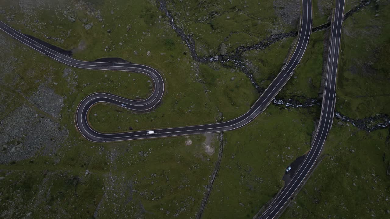 Aerial shot ascending from Transfagarasan road in Romania, circling upward through white clouds. Cars driving. Cinematic and moody nature.