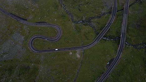 aerial shot ascending from transfagarasan road in romania, circling upward through white clouds. cars driving. cinematic and moody nature.