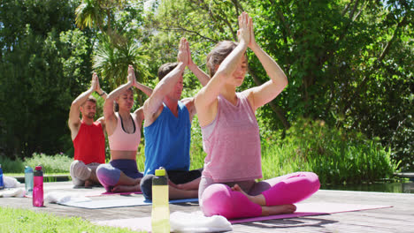 Diverse-male-and-female-group-practicing-yoga-sitting-in-a-row-on-mats-in-sunny-park